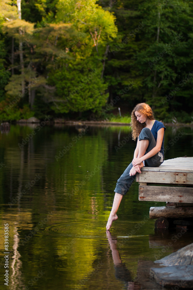 pretty teen girl on a lakeside dock in summer