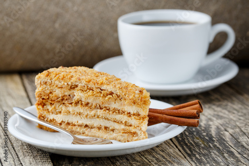Tasty honey cake with cup of coffee on wooden background.