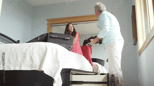 A man and woman unpack their bags which are resting on the bed