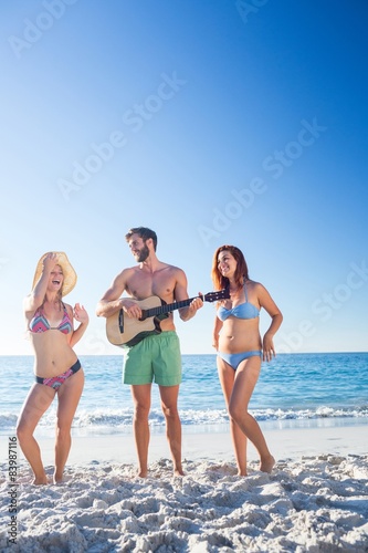 Handsome man playing guitar and his friends dancing