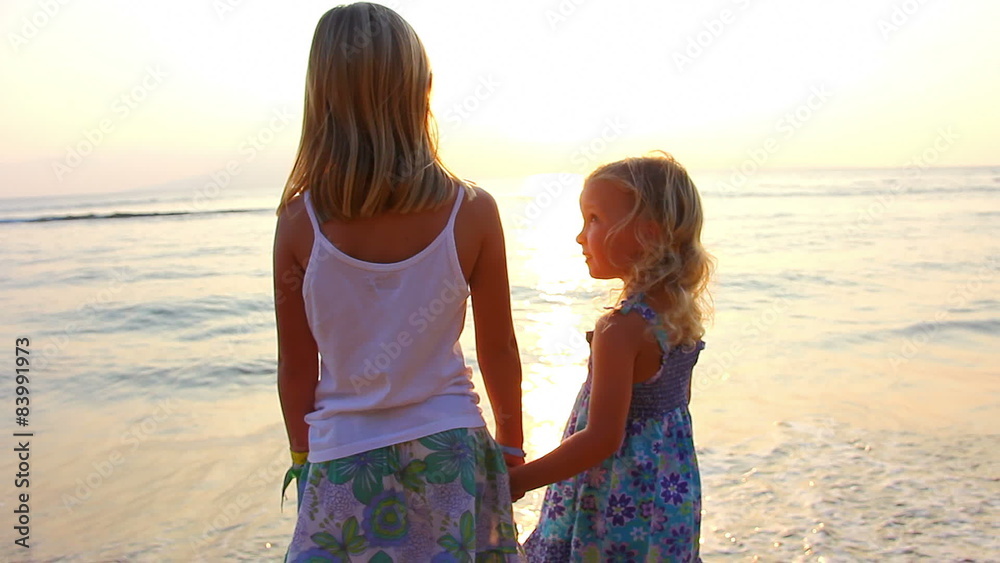Two sisters hug each other while on the beach with the sun setting behind them Two sisters hug each other while on the beach with the sun setting behind them
