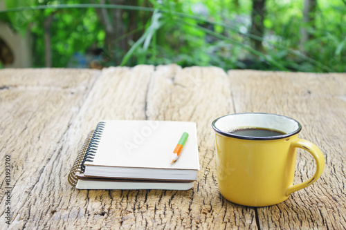 Notebook and coffee in yellow cup on wooden table