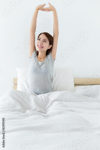 Young woman waking up and stretching hand on bed
