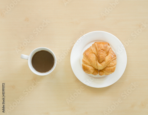 Croissant on white plate and cupof coffee.