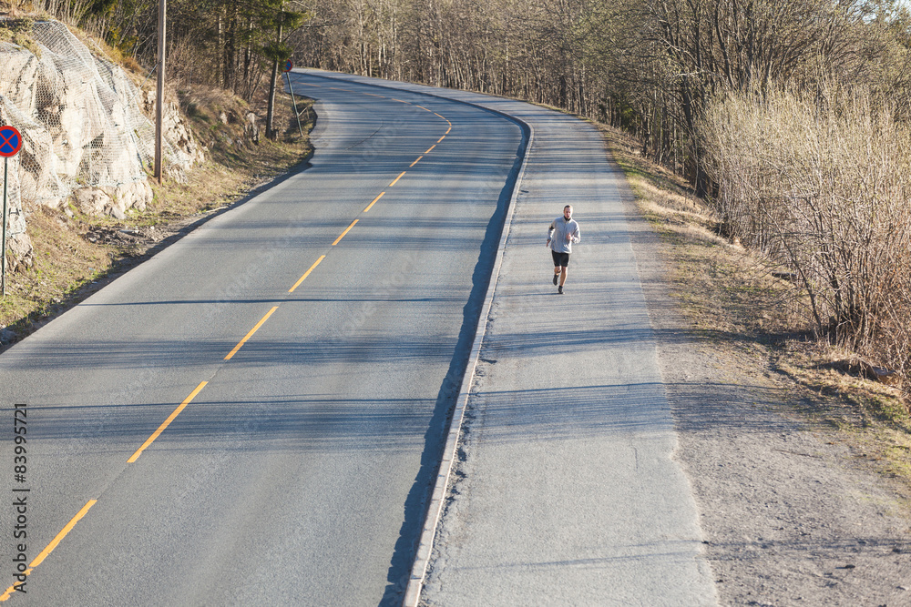 Young man running outside along an empty mountain road