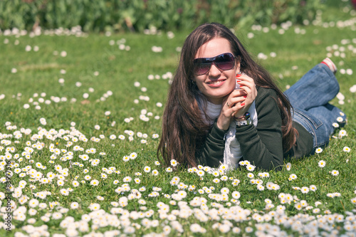 Girl in sunglasses enjoys the spring sun on the lawn of daisies