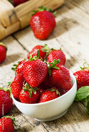 Fresh strawberries in a white porcelain bowl on wooden table in