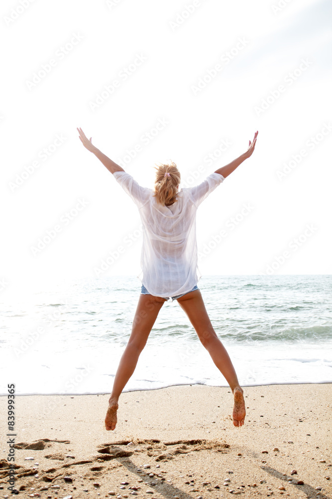 Excited young woman jumping with hands raised on beach Excited young woman jumping with hands raised on beach