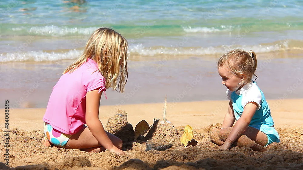 Two adorable little girls wave at the camera while playing in the sand together Two adorable little girls wave at the camera while playing in the sand together