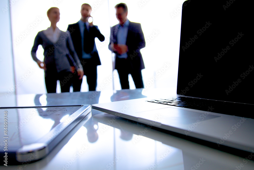 Laptop computer on desk , three businesspeople standing in the Laptop computer on desk , three businesspeople standing in the