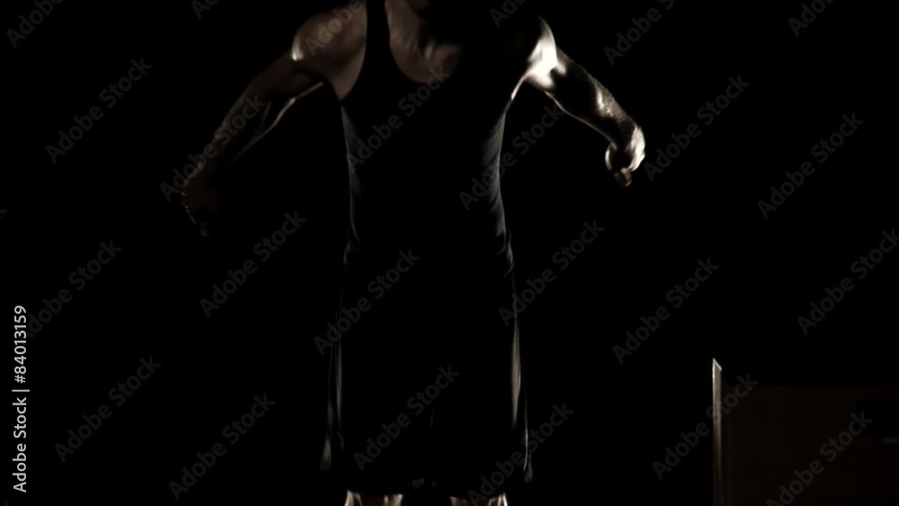 Athlete jumps up and down intensely, on a box in a darkly lit room
