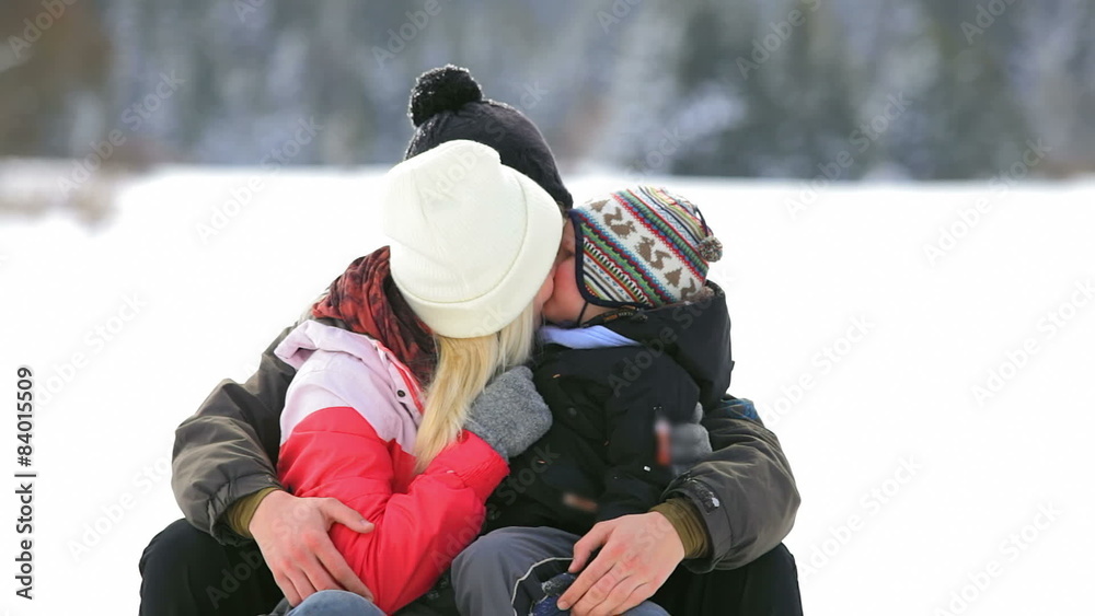 A young couple with a little boy sit in the snow and kiss A young couple with a little boy sit in the snow and kiss