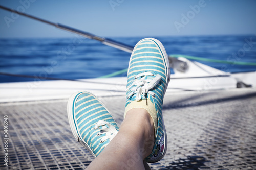 woman lounging on a catamaran sailboat trampoline with her feet propped up and crossed. © lusia83
