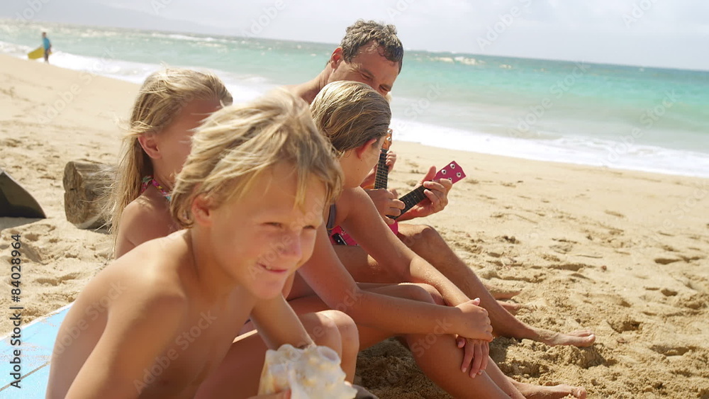 A family sits in the sand at the beach and play ukulele and blow conch shells