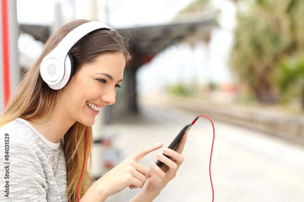 Teen girl listening to the music with headphones waiting a train