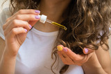 Young girl caring for curly hair tips with yellow oil
