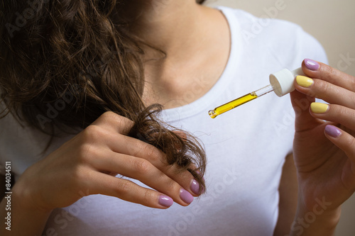 Принти на полотні Young girl caring for curly hair tips using a  oil