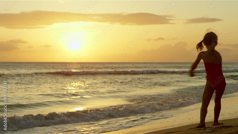A cute little girl dances and twirls on the beach at sunset A cute little girl dances and twirls on the beach at sunset