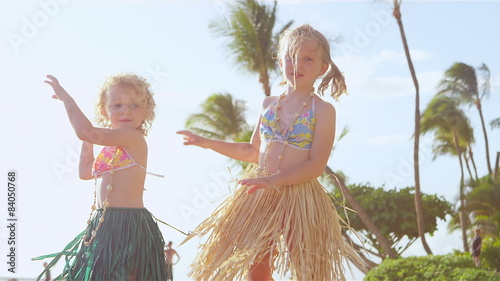 Two young sisters stand and show off their hula dance moves