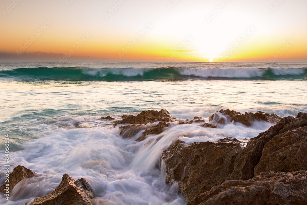 Early morning landscape of ocean over rocky shore and glowing su