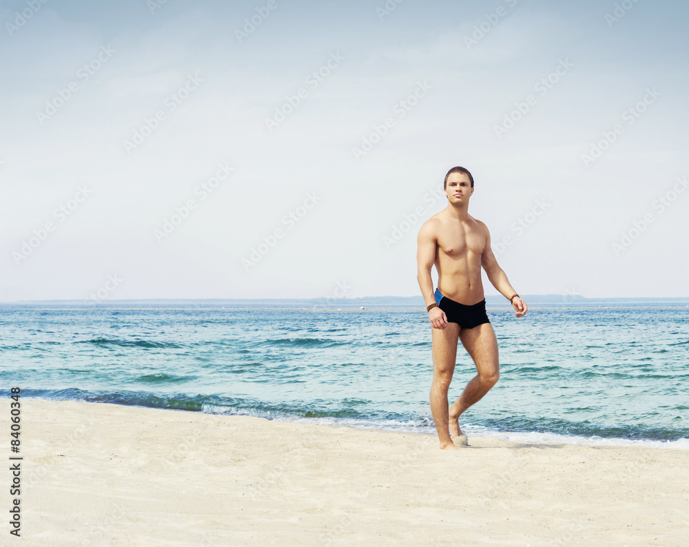 Young, fit and handsome man with athletic and muscled body walking on a summer beach Young, fit and handsome man with athletic and muscled body walking on a summer beach
