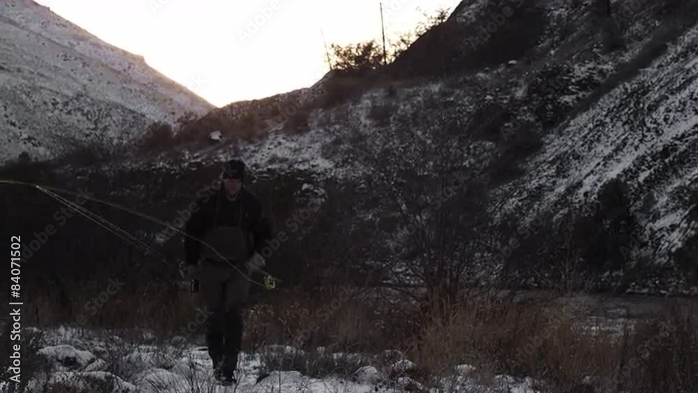 A man hikes down a snow covered trail while holding two fishing poles A man hikes down a snow covered trail while holding two fishing poles