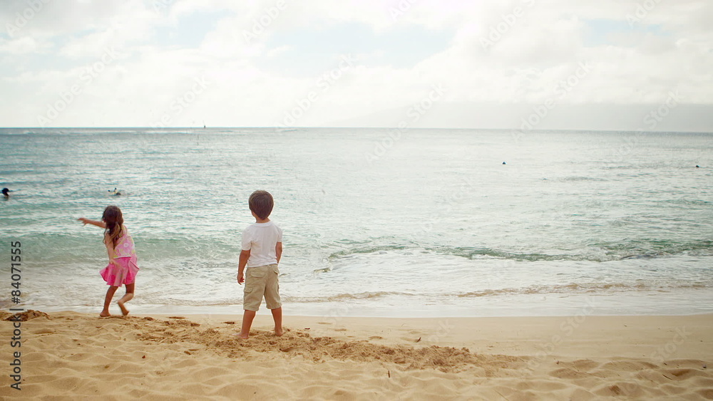 A young boy and girl stand and throw sand into the ocean A young boy and girl stand and throw sand into the ocean