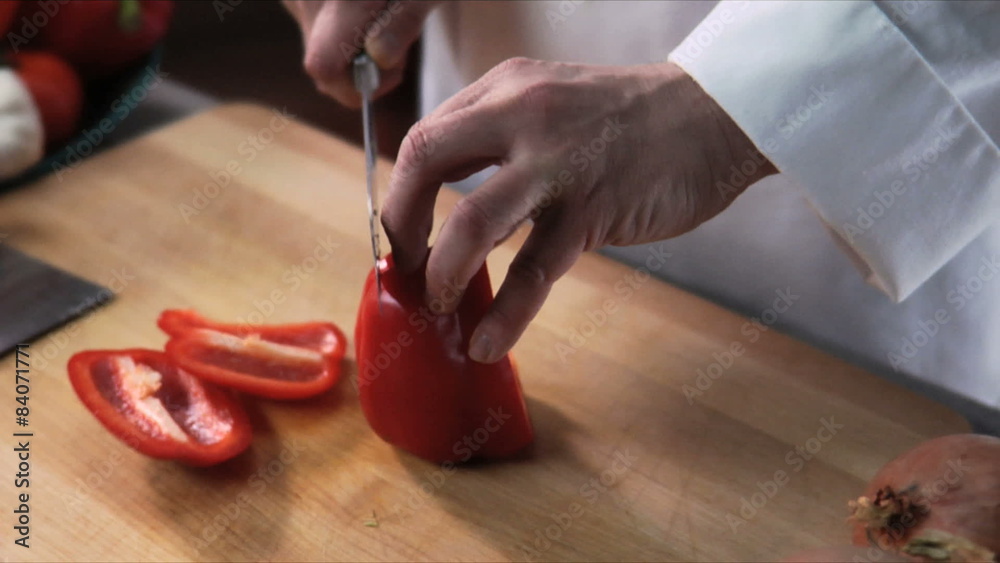 Close up of a chef slicing a red bell pepper on a wooden cutting board