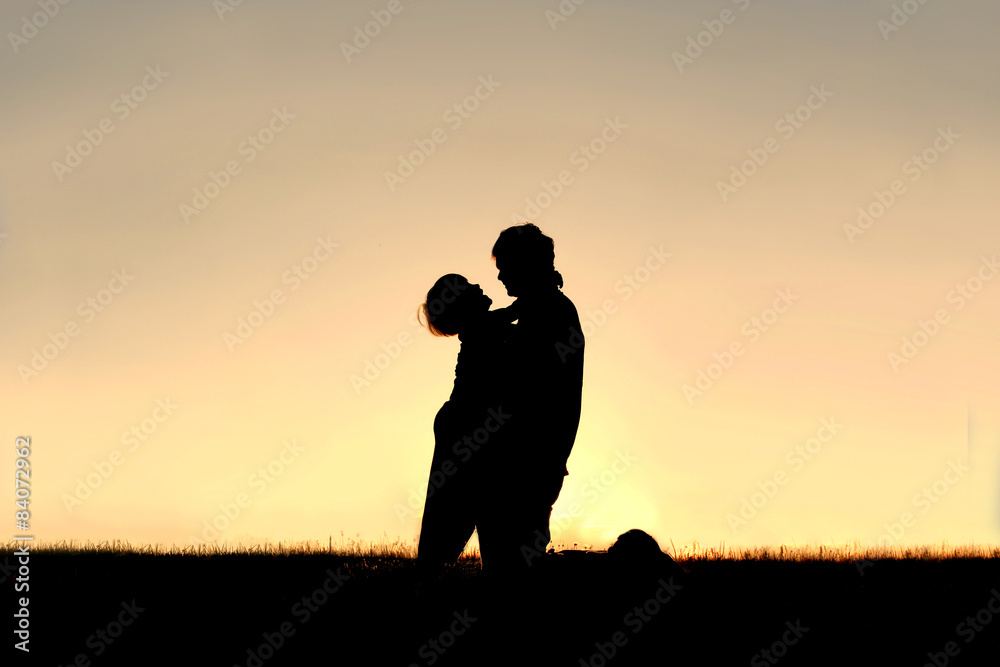 Silhouette of Child Laughing and Hugging Father at Sunset