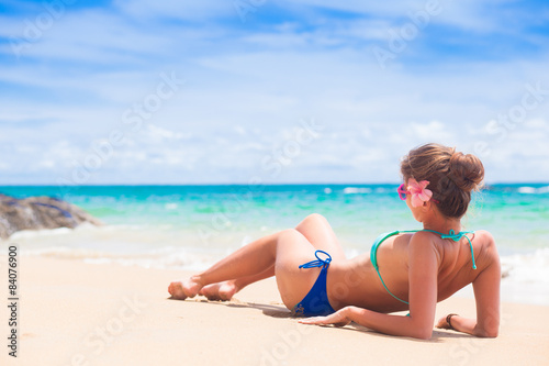 woman in bikini and flower in hair and sunglasses lying on