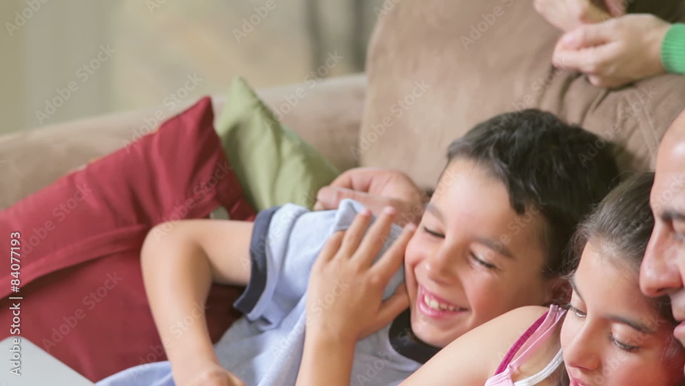 Mother looks over the couch on father as he reads a tablet with his kids Mother looks over the couch on father as he reads a tablet with his kids