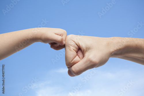 father and son punching fists for agreement on sky background © TheMagicalLab