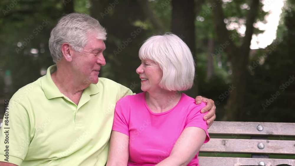 Affectionate senior couple sitting on a bench look at one another. Medium shot.