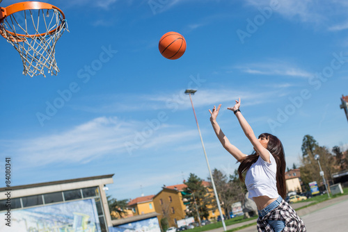 Young casual woman throwing basketball ball outdoors in a sunny
