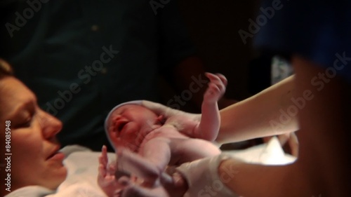 Newborn baby being held up and handed to its mother.