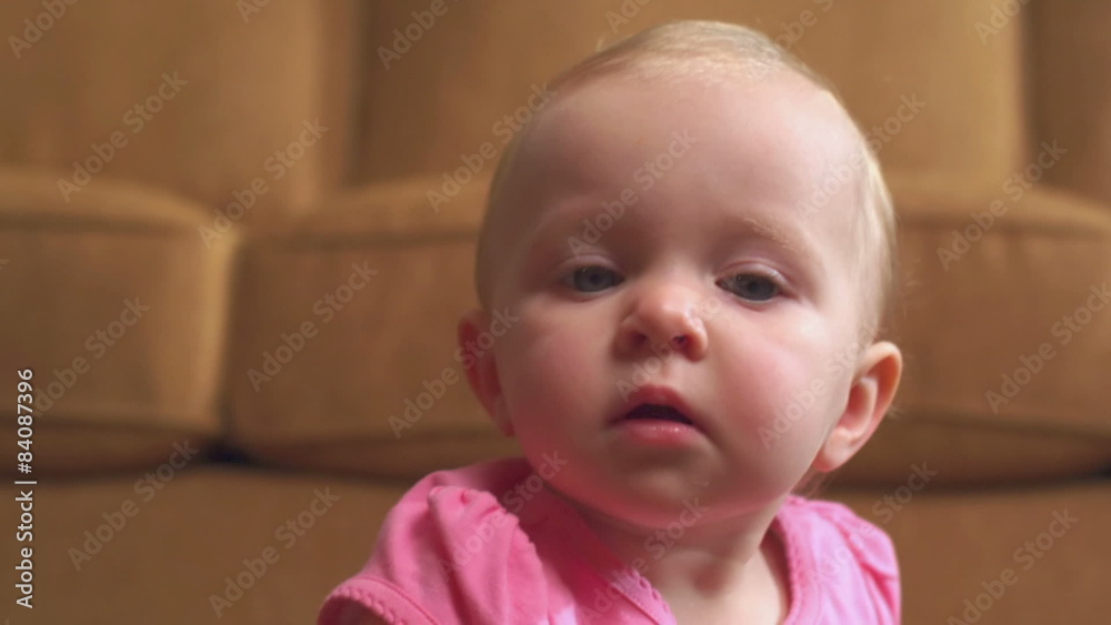 A baby girl sits on the floor in front of the sofa and looks up in front of the camera A baby girl sits on the floor in front of the sofa and looks up in front of the camera