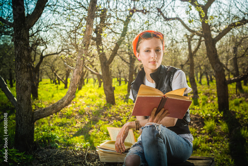 Woman in park outdoor with tablet and book deciding what to use