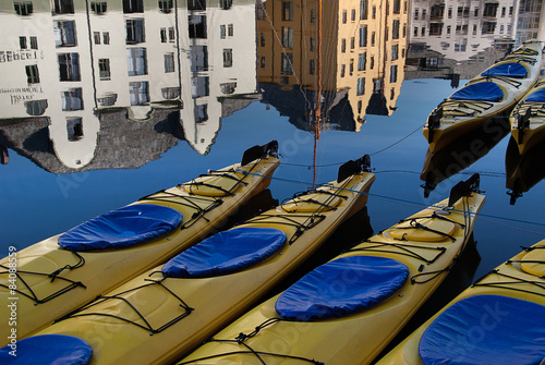 Close up of kayaks docked in Brosundet, Ålesund, Aalesund, Norway. Beautiful Jugend buildings in the background reflected in calm sea. Yellow blue white.