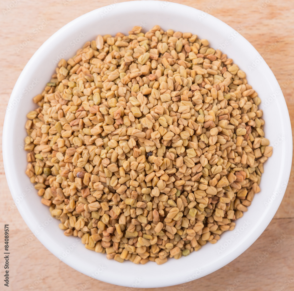 Fenugreek seeds in white bowl on wooden surface Fenugreek seeds in white bowl on wooden surface