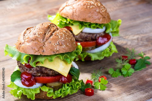 Big hamburger with beef cutlet and vegetables on wood background