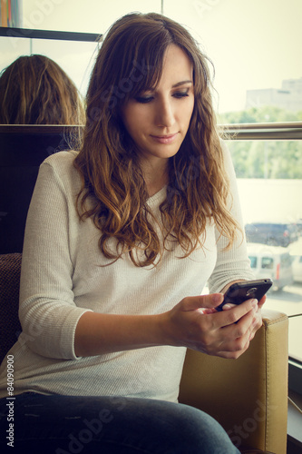 Young cheerful woman sitting in restaurant using smartphone.