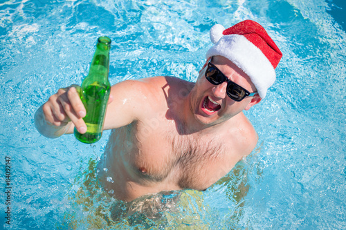Photography Man with santa hat partying in pool with beer bottle in hand
