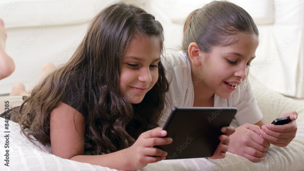 Girls lie on the floor and play with a tablet computer and a cell phone