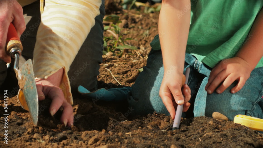 A Grandmother and her granddaughter dig a hole for a flower with trowels.