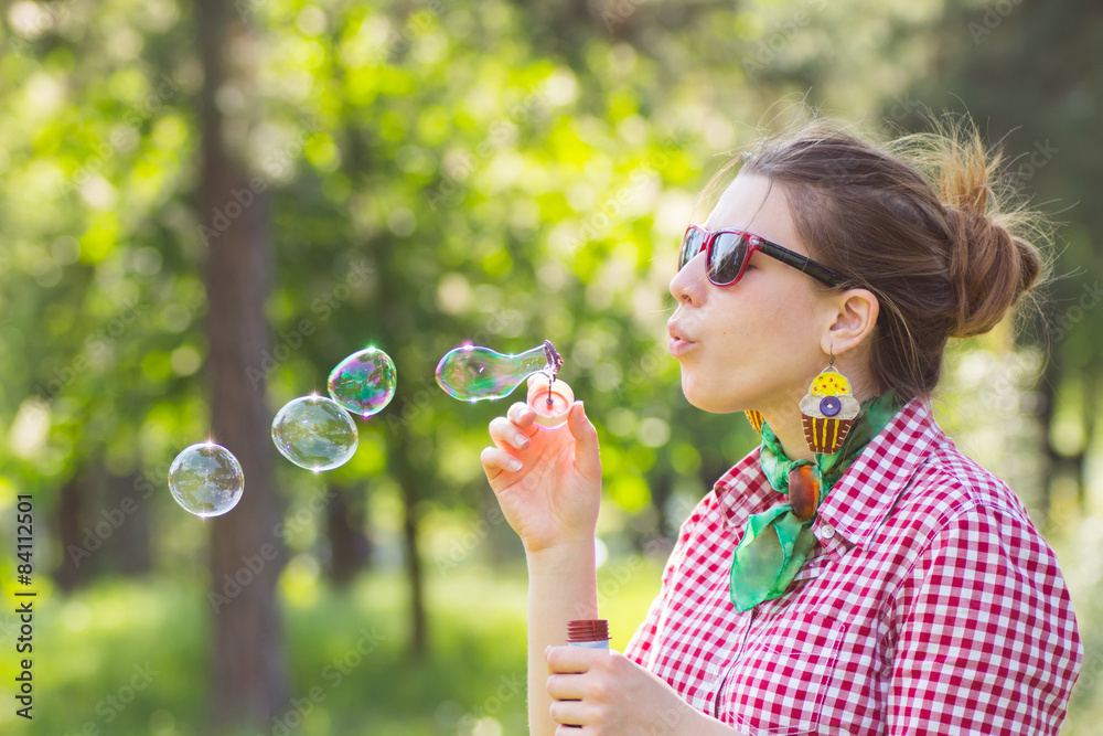 Cheerful beautiful brunette girl in glasses blowing soap bubbles