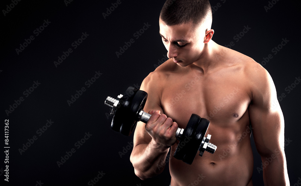 Young man with bare chest lifting dumbbells on black background.