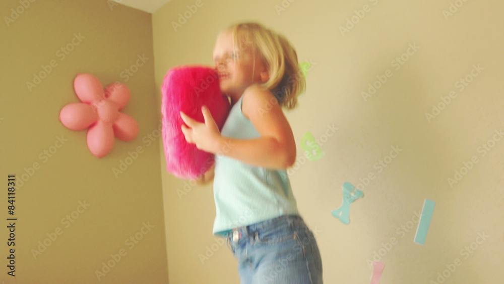 A young girl jumps on her bed and hugs a pink fuzzy heart shaped pillow