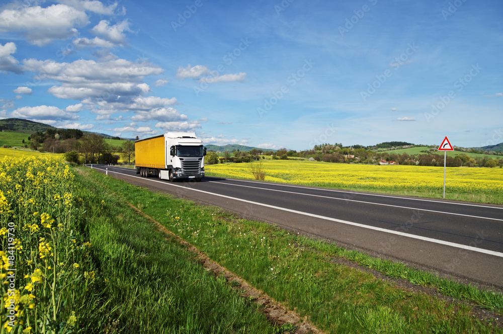 Truck on the road between yellow flowering rapeseed field