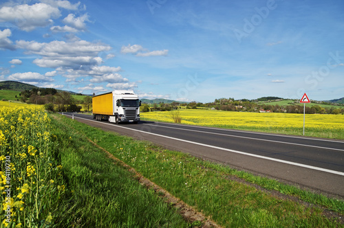 Obraz na płótnie Truck on the road between yellow flowering rapeseed field w salonie