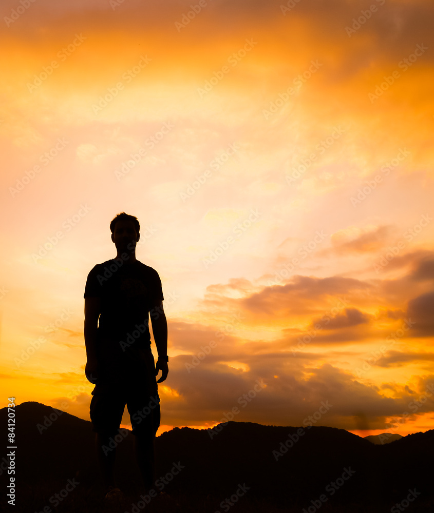 Silhouette of man standing on mountain with dramatic golden sky on background
